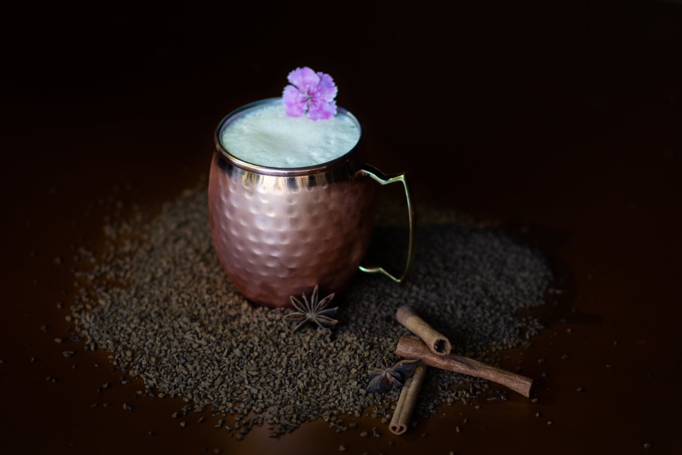 taza de café en coctel con varitas de canela y una flor morada en fondo negro