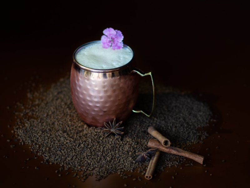 taza de café en coctel con varitas de canela y una flor morada en fondo negro