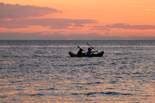 two people in a kayak paddling in the sea at sunset