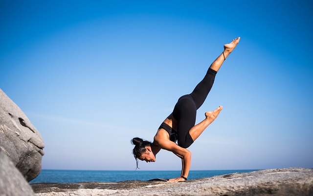 woman performing a yoga pose in front of the sea on a rock and background sky